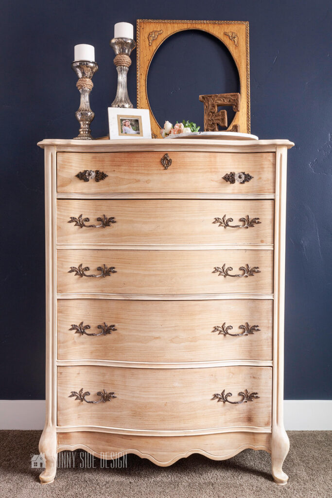 The beautifully restored natural wood finish dresser with the original antique hardware in a bedroom with a navy blue accent wall.
