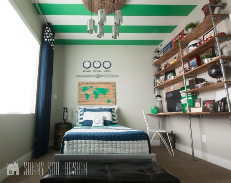 Tween boy bedroom with green and white striped ceiing, navy blue curtains, metal industrial bed with blue and white striped bedding, industrial pipe wall shelf with built in desk area.