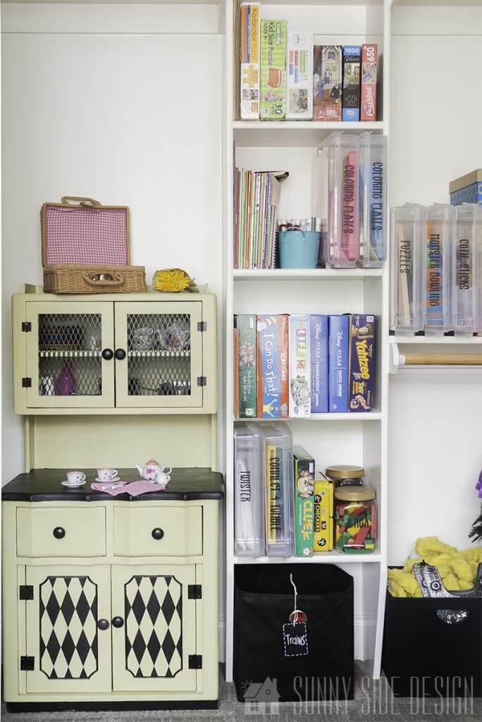 Organize toys in closet area of playroom with clear labeled storaged bins stacked neatly on shelves. Also in the closet is a play kitchen with food and dishes organized in cupboard.