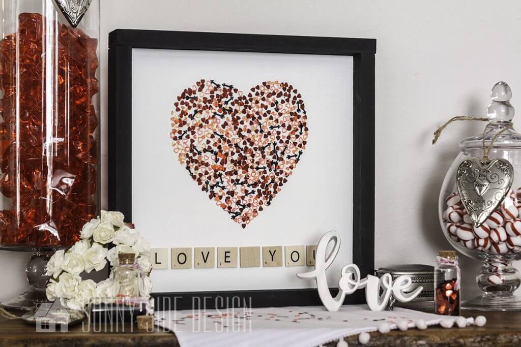 Confetti Heart Shaped Valentine decor in a Farmhouse frame on a table with love sign, apothacary jar with candy and white rose heart wreath.