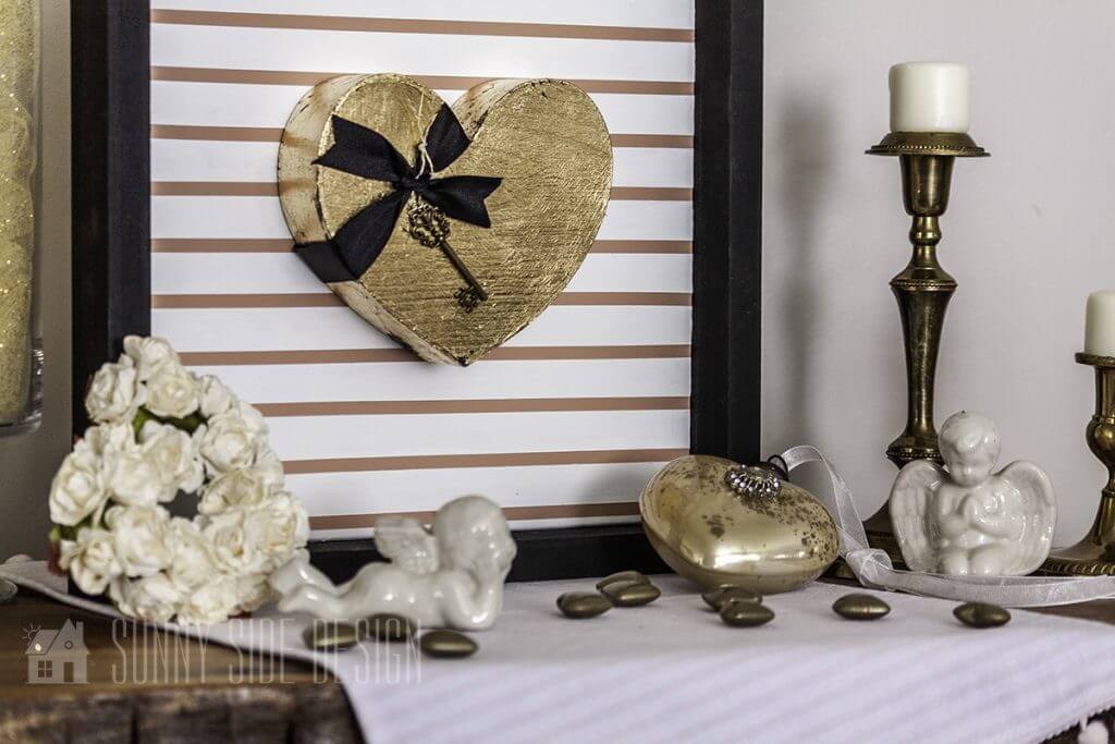 Easy Valentine's Day decor with a gold leaf heart mounted on a blush and white pin stripped frame with other various hearts and white cherubs.