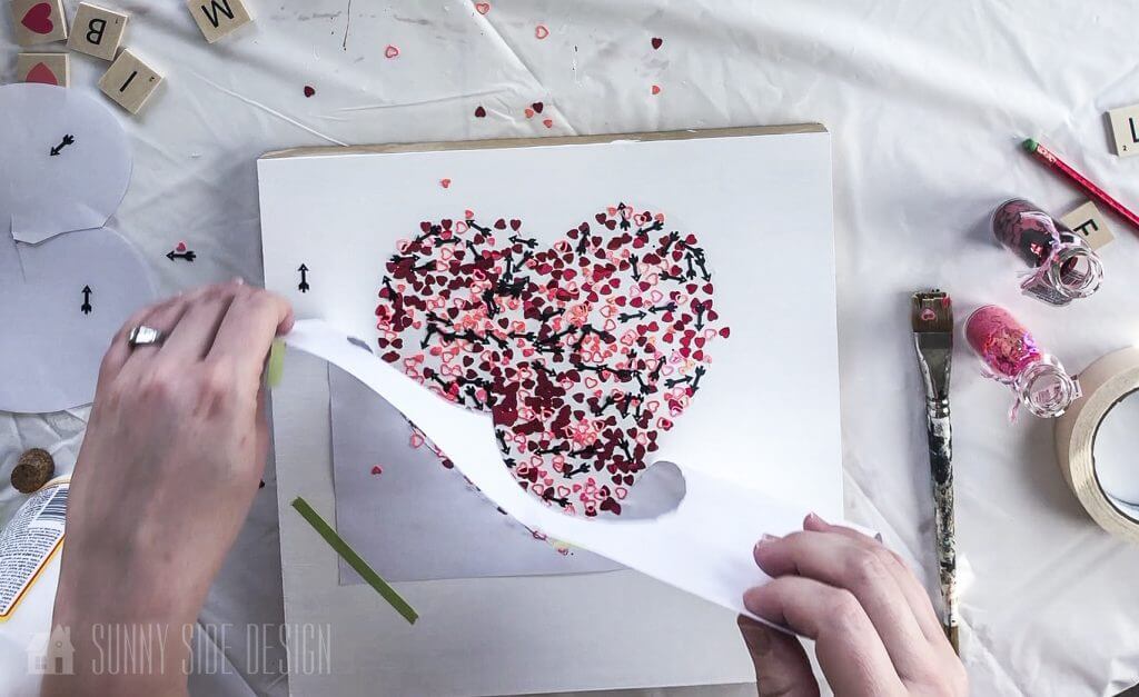 Woman's hand removing heart stencil from Valentine decor.