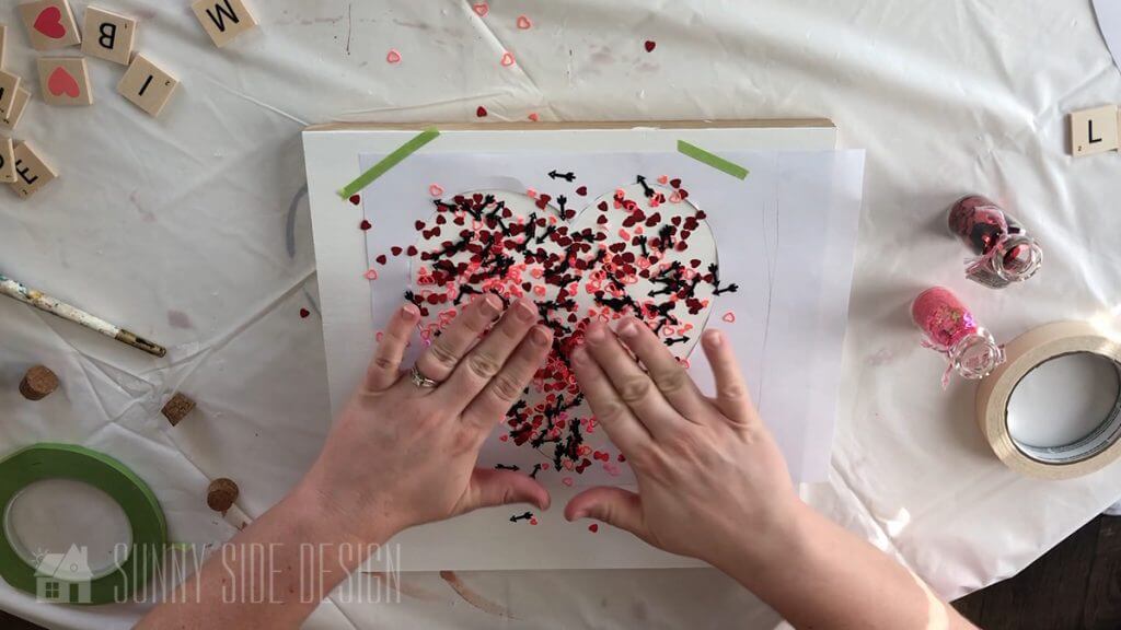 Woman's hand pressing confetti onto the mod podge in a heart shape