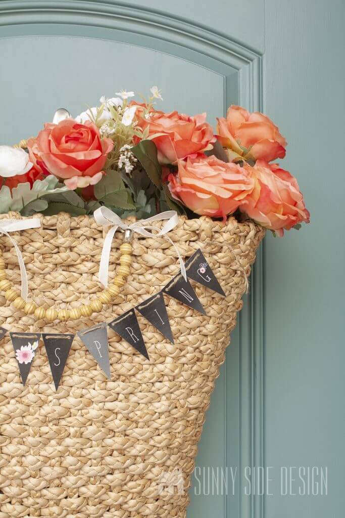 Basket full of flowers with a small spring banner printable "hello spring" on a blue door.