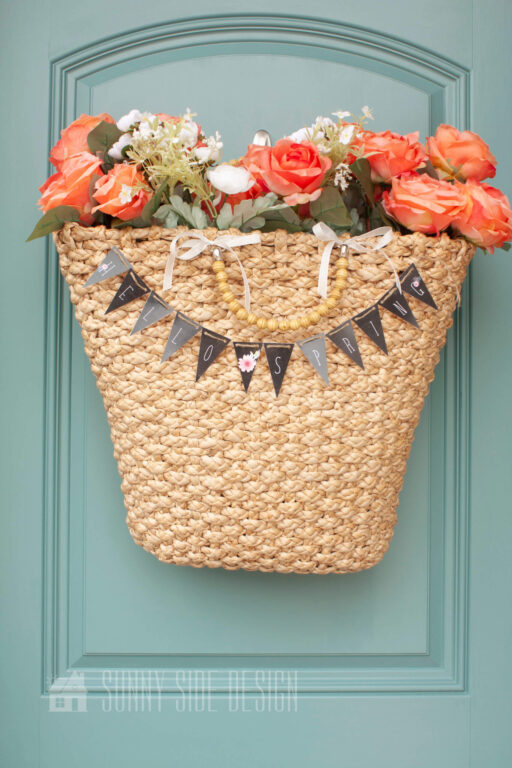 Basket full of flowers with a small spring banner printable "hello spring" on a blue door.