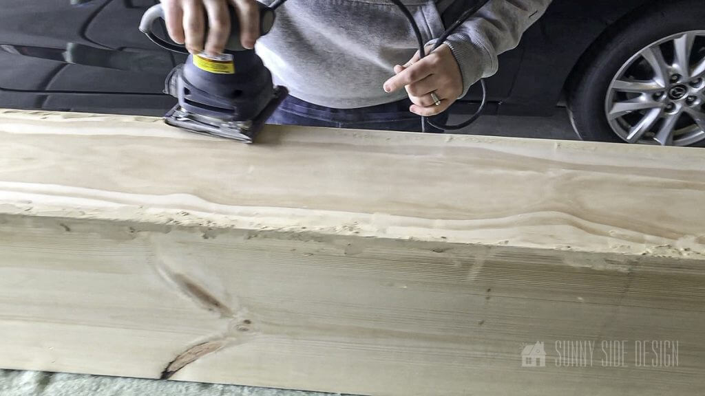 Using a palm sander excess wood filler is removed from the faux mantel beam.