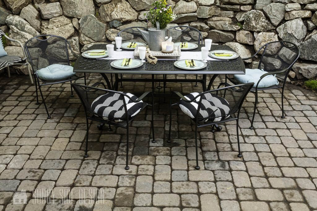 Dining area in outdoor living space with black metal dining set, aqua, black and white  striped cushions. Table is set. for an evening dinner al fresco.