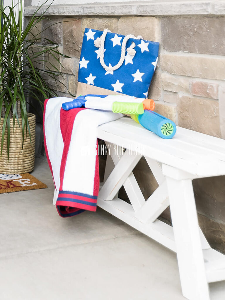 Simple white farmhouse DIY 2x4 bench on a front porch, styled with summer decor.