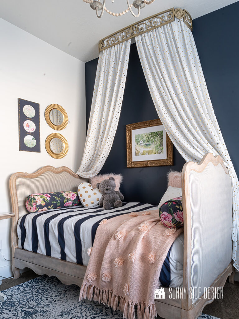 Beautiful upholstered French country daybed upcycled from a pair of twin beds. Styled with a bed crown, blue and white striped bedding with blush accent pillows.