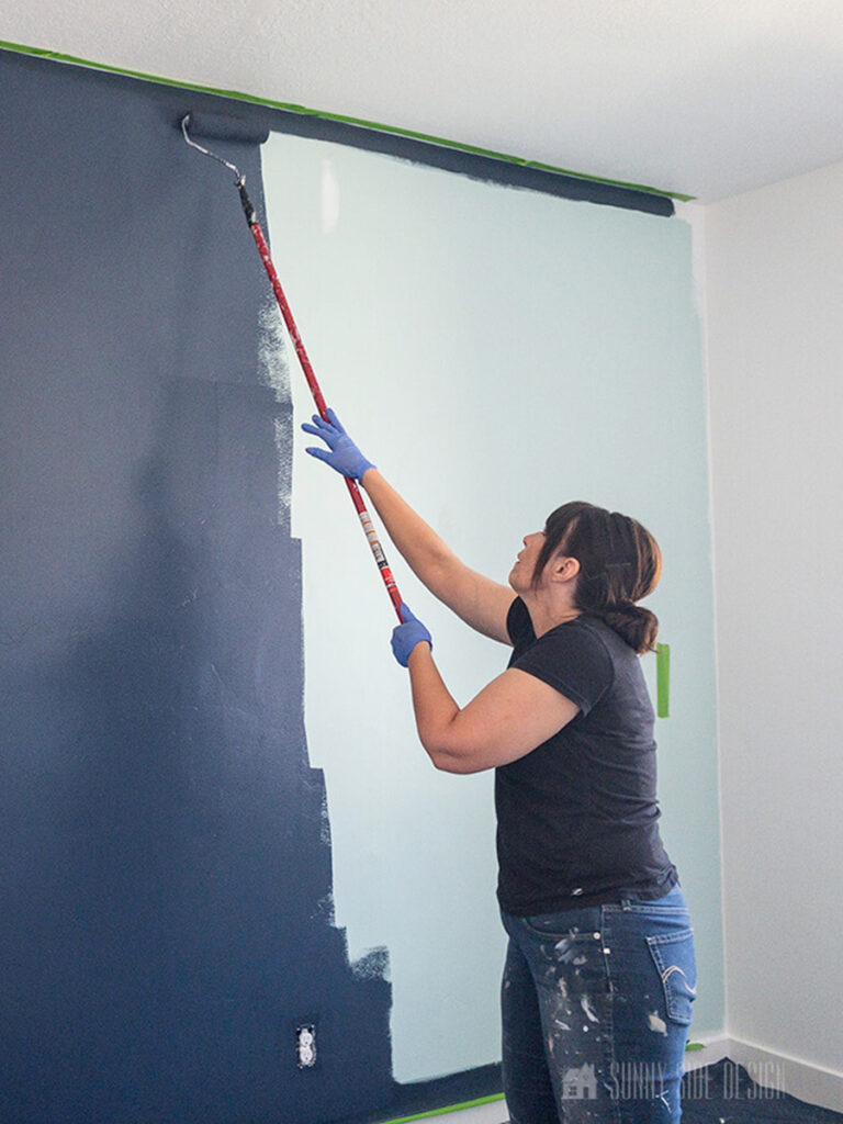 Woman rolling on navy blue paint for an accent wall with tips on how to paint a room with pro results.
