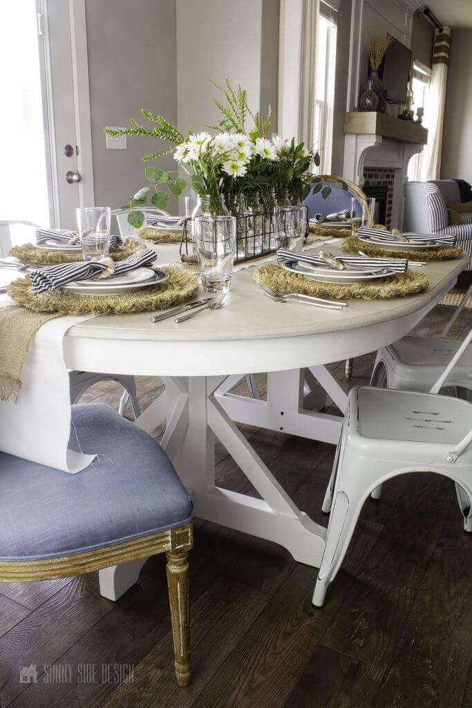 Flea market flip ideas, road side table gets a makeover with white chalk paint and a natural wood finish on the top. Light blue upholstered chairs with white farmhouse stile metal chairs. Table is set with straw placemats, navy and white dished and napkins. White floral centerpiece