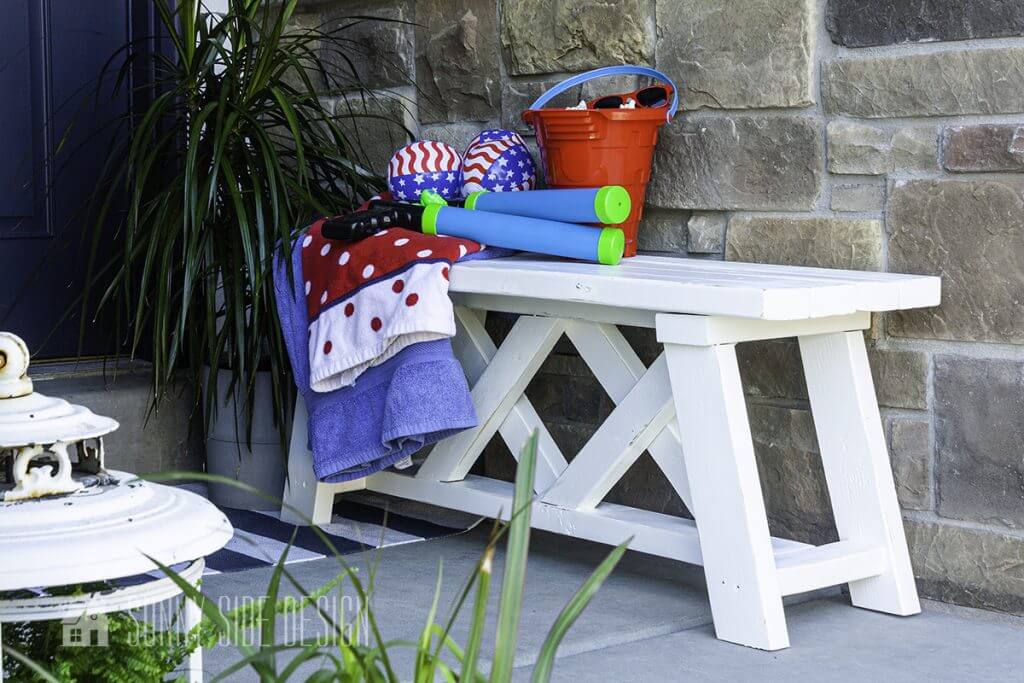 Simple white Farmhouse 2x4 bench on a small front porch styled with a red, white and blue beach towel, water guns and a sand bucket.