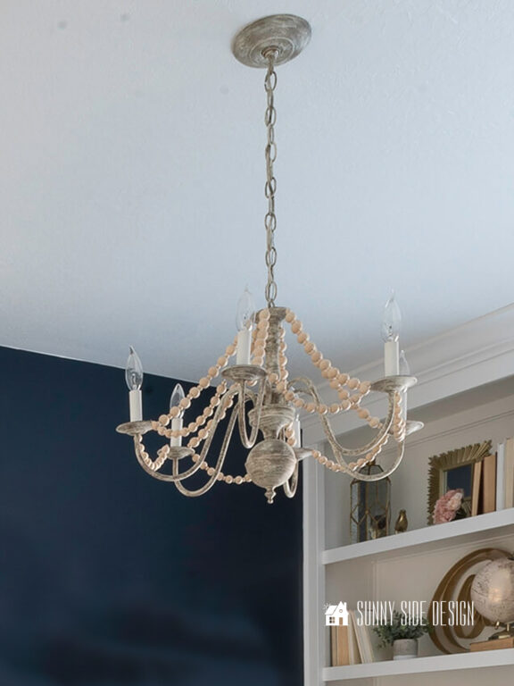 Easy French country chandelier hanging in a girls bedroom with a navy blue accent wall and built-in shelves.