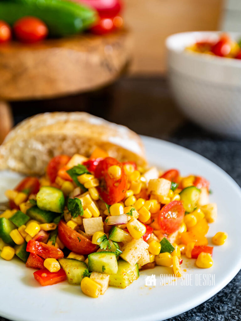 Corn salad served on a plate with a slice of crusty bread, perfect side for summer entertaining.