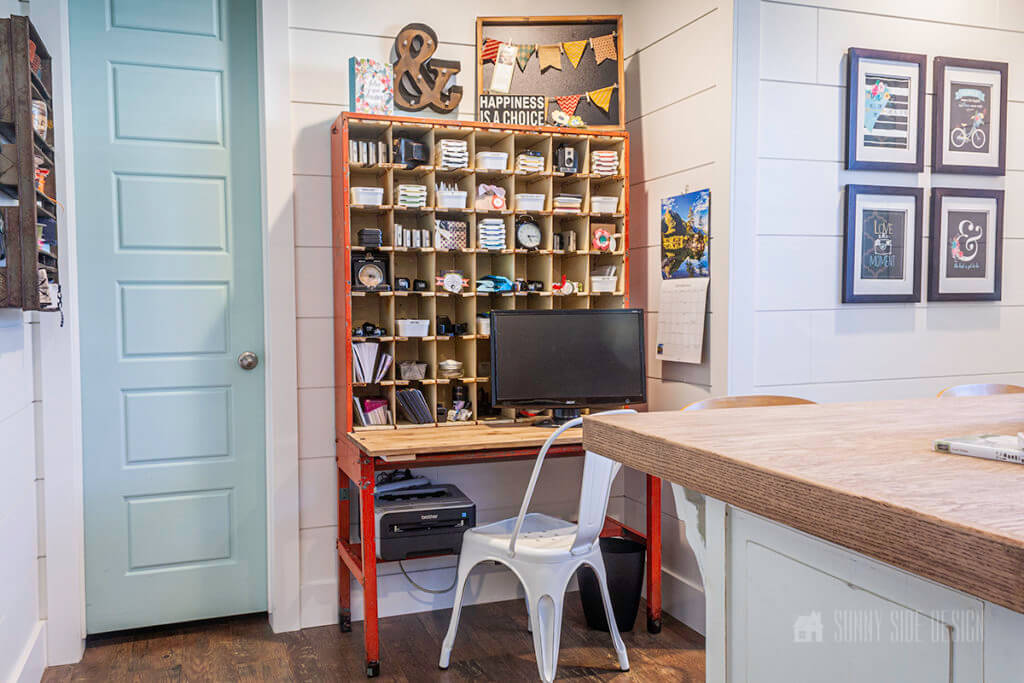 Select furniture that reflects your style: a vintage orange postal sorter is upcycled into a desk for a computer station with a white metal chair, aqua door and white shiplap walls.