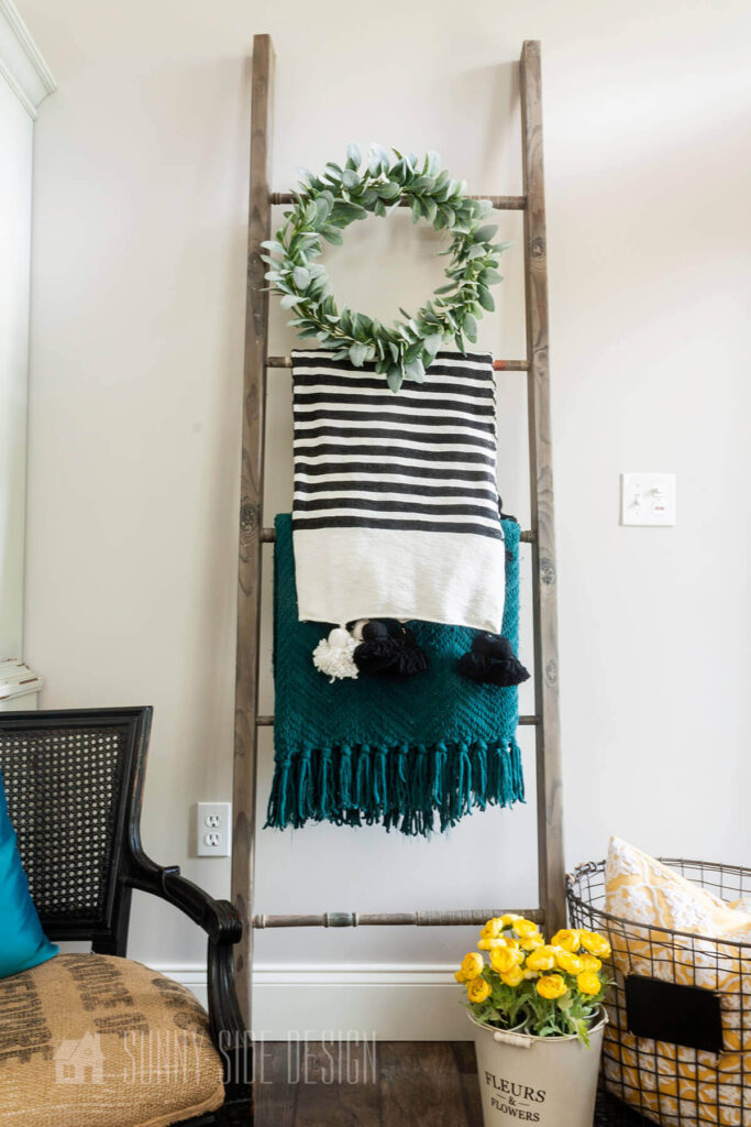 A blanket ladder made with scrap lumber and croquet mallet handles, staked with blankets and a wreath.