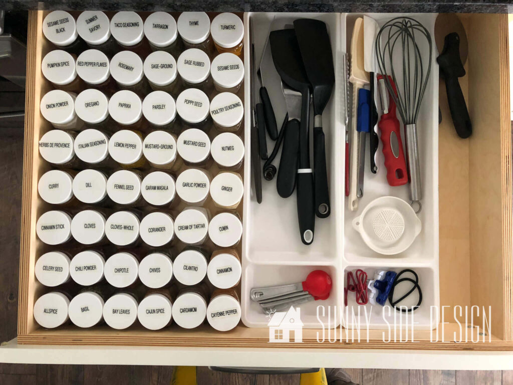 Kitchen drawer organized with alphabetized spices and utensils organized in white sorters.