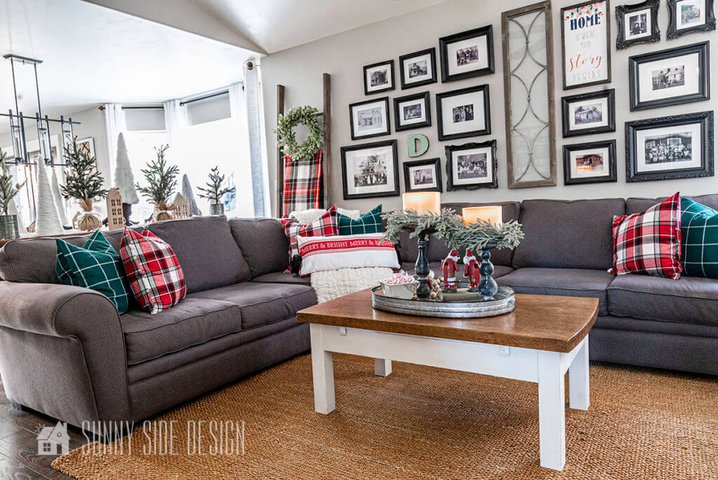Grey sectional decorated with green and red plaid flannel pillows and a chunky white throw blanket. Coffee decorated with a galvanized tray filled with 2 farmhouse style candlesticks, candles and a pine candle ring.