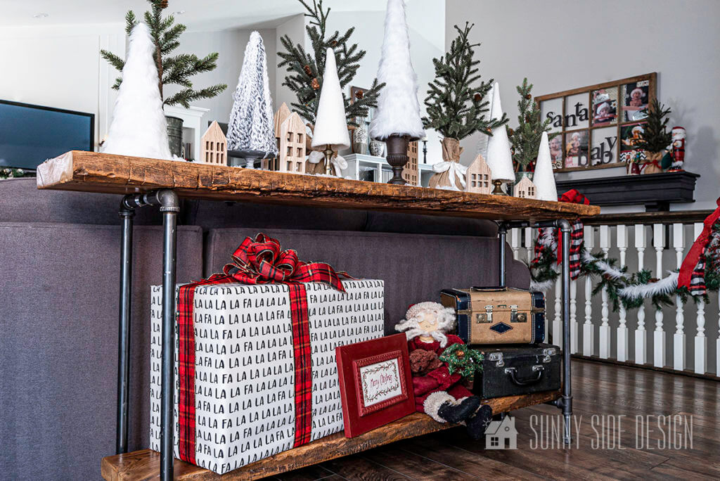 Christmas Decorating Ideas, sofa table decorated with wrapped Christmas gift, Santa, and a collection of cozy and pine tree decor.