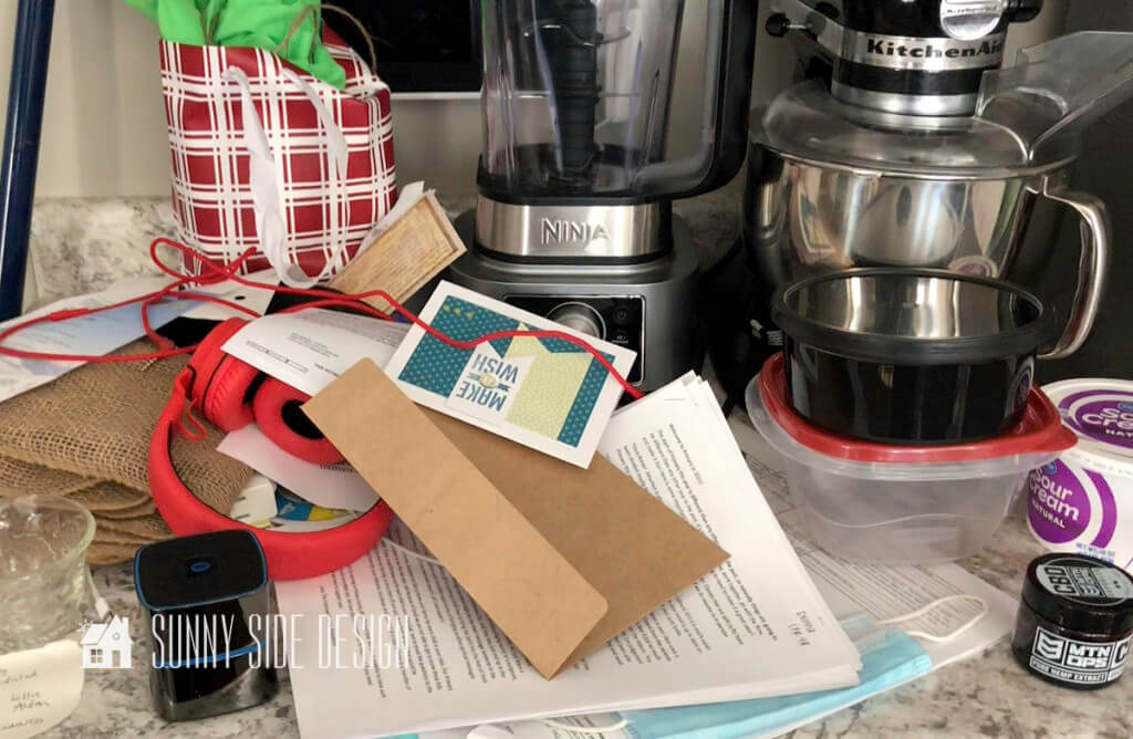 Kitchen counter top covered in clutter, invitations, envelops, gift gabs, appliances, school papers, ets.