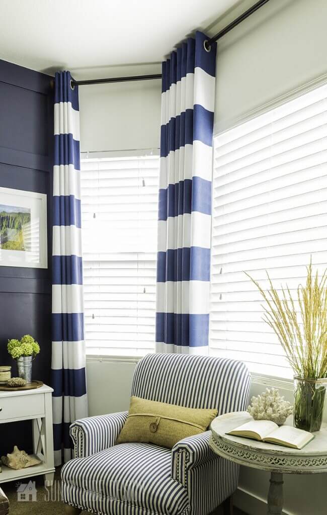 DIY curtain rod for bay window, easy DIY for beginner project. Black curtain rod with navy and white striped curtain, blue and white stripped chair with a light grey accent table with a vase of grasses.