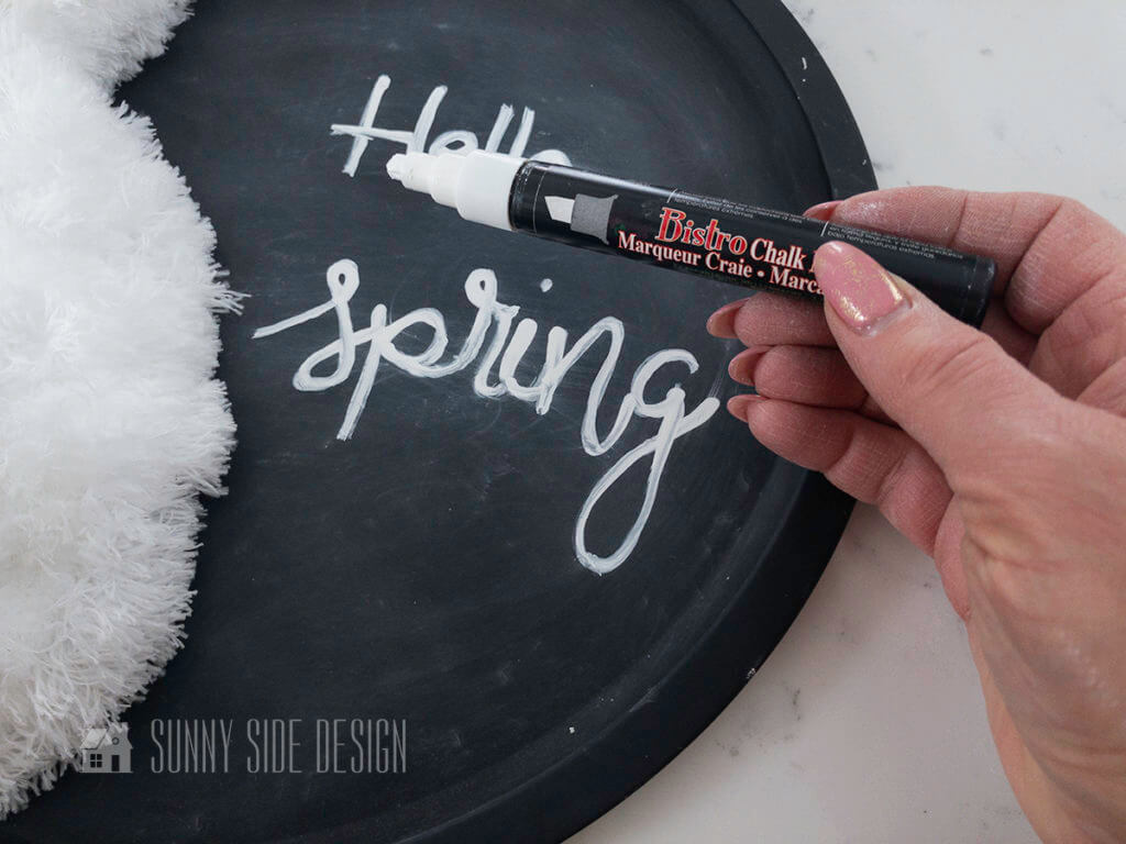 With a white chalk marker, write the words "Hello Spring".