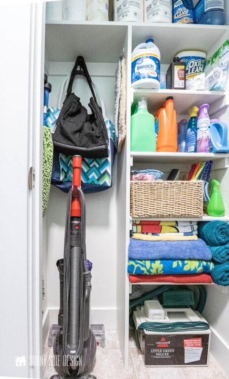 Organized broom closet with vacuum, mop, extra towels and cleaning supplies.