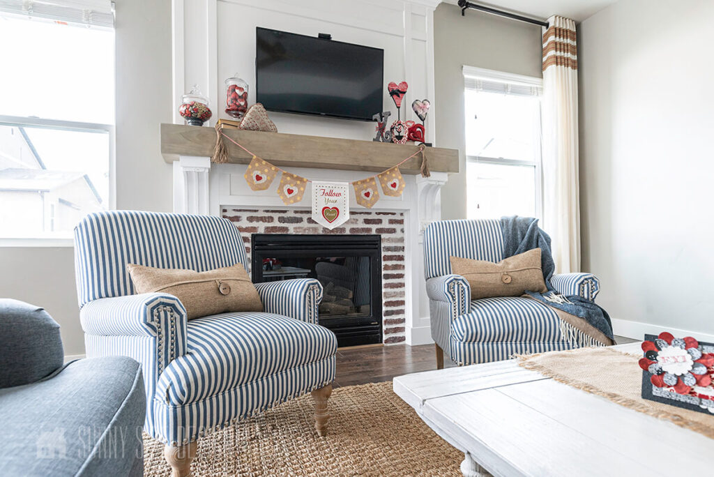 Fireplace mantle styled with Valentine Day decor with 2 blue and white striped chairs.