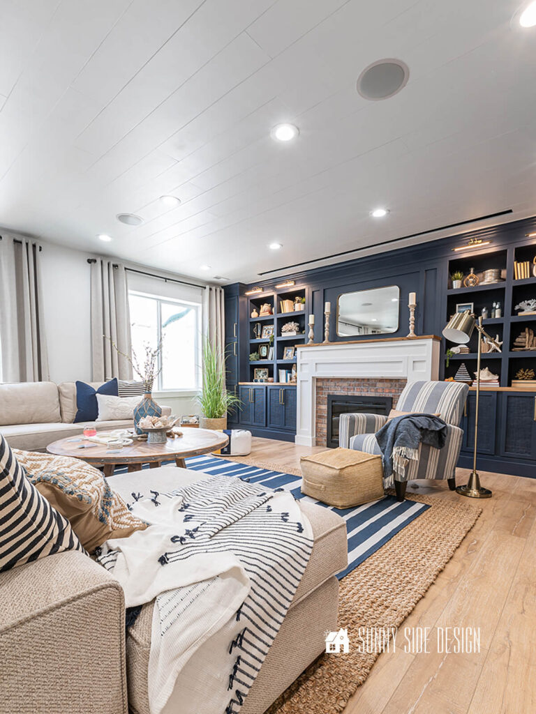 Completed shiplap ceiling in a basement family room. With navy blue built-ins, oak floors, off white sectional and a navy and white rug layered over a sisal rug.