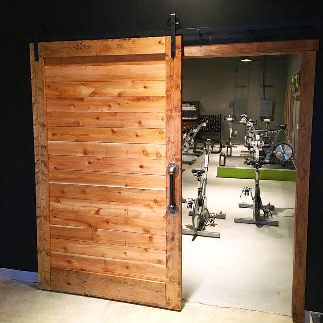 Rustic wood sliding barn door installed at a fitness gym, mounted with black hardware, black painted wall.