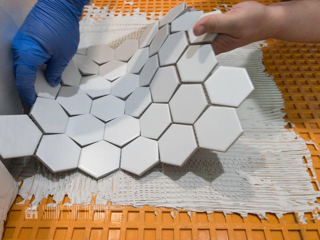 placing first tile into place parallel to the bathtub