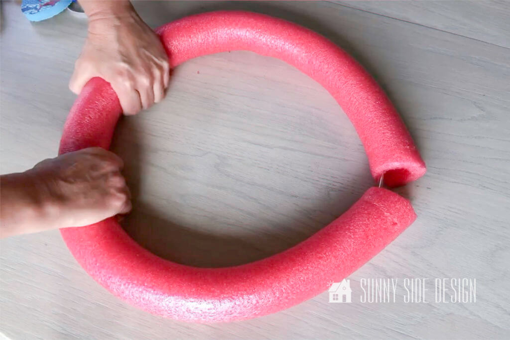 Woman's hands shaping red pool noodle into a circle for the summer wreath for front door.