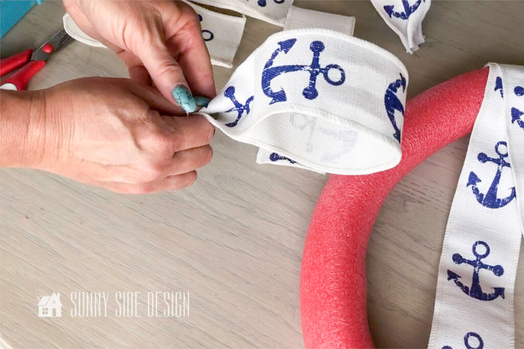 Woman's hands forming a bow for the summer pool noodle wreath with the nautical ribbon.