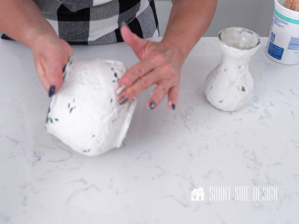 Woman's hands smooth plaster on a glass vase, creating DIY decor for home.