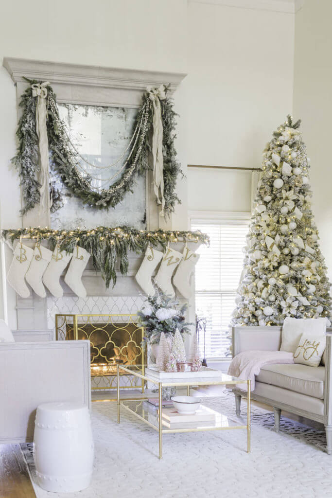 White flocked Christmas tree with white ornaments, white ribbon, white poinsettias. Fireplace mantle is also decorated with white flocked greenery, white ribbons, and white stockings. in a white living room.