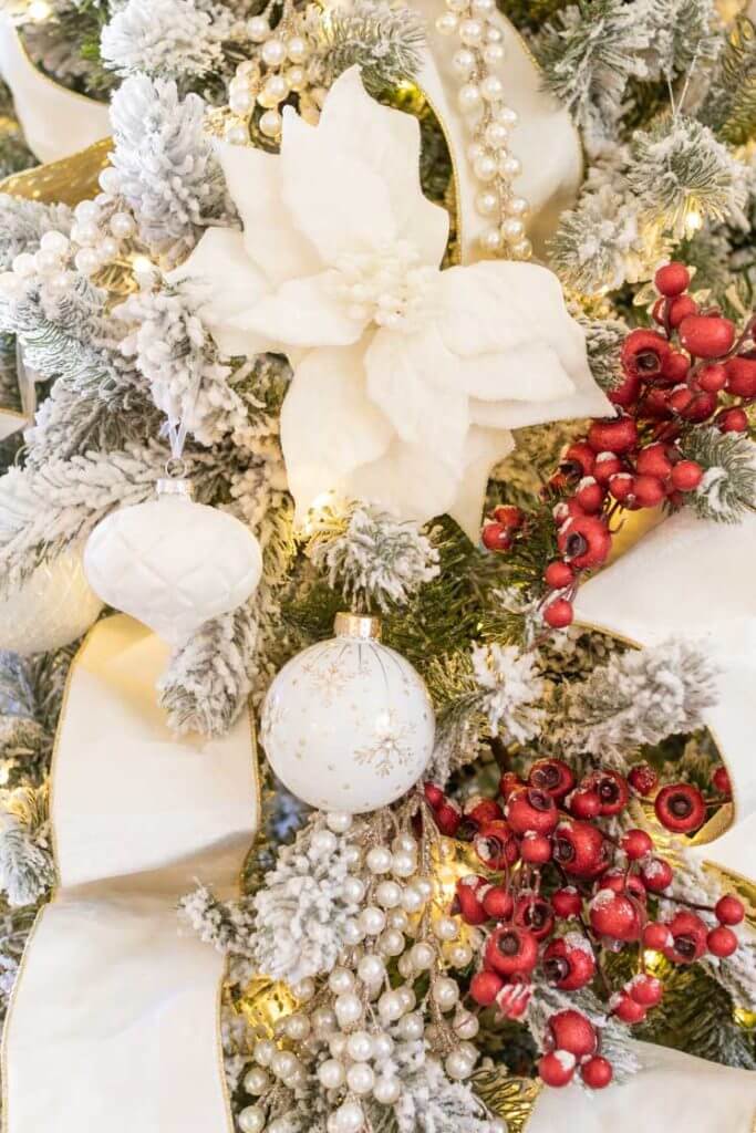 Red berried on a white flocked Christmas tree with white ornaments, white poinsettias, and white ribbon.