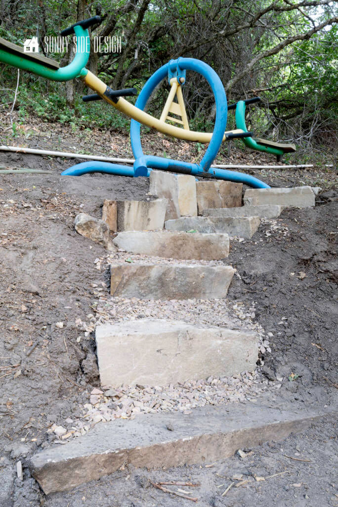 Outdoor Stone Steps on a slope, made with stacked stone and flagstone chips. ground cover flanks the steps leading to a teeter totter.