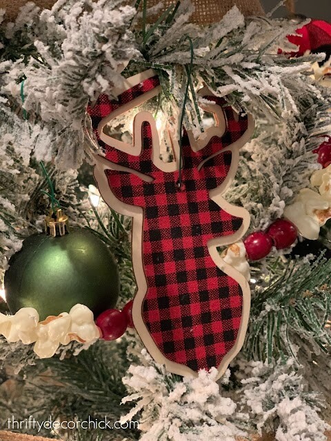 Close up view of red and black buffalo checked reindeer ornament on a white flocked tree with a popcorn and cranberry garland.