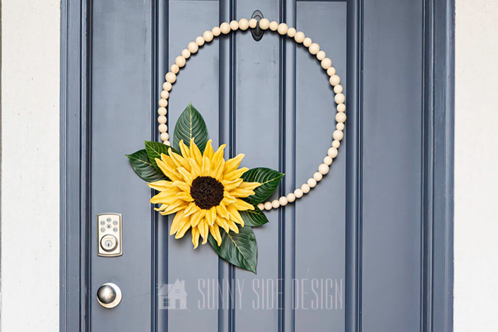 Natural wood bead modern wreath with a giant yellow sunflower hanging on a navy blue door.