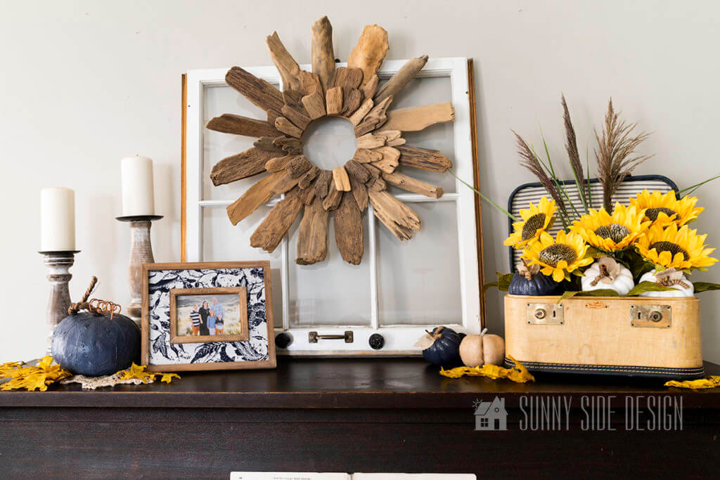 Fall decorations on top of the piano. Starting on the left 2 rustic candlesticks, a navy blue pumpkin, maple leaves and a family photo. Center is a driftwood wreath and on the right a simple sunflower arrangement. with pumpkins and maples scattered around.