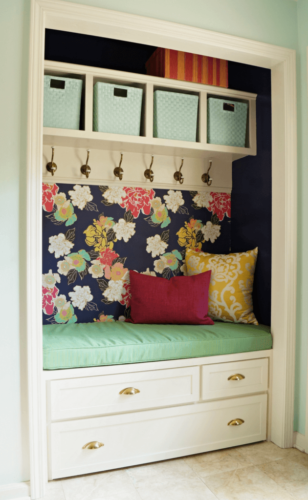 Mudroom idea in a laundry room with a pretty wallpaper wall and upholstered bench.