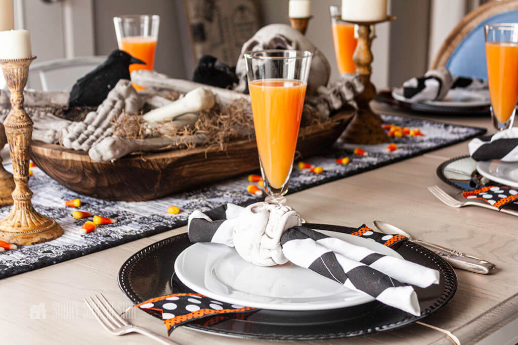 DIY dollar tree skull napkin rings on a spooky set table with orange drink in goblets.