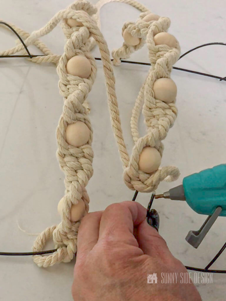 Woman's hand Applying hot glue to cut edge of wire wreath frame.
