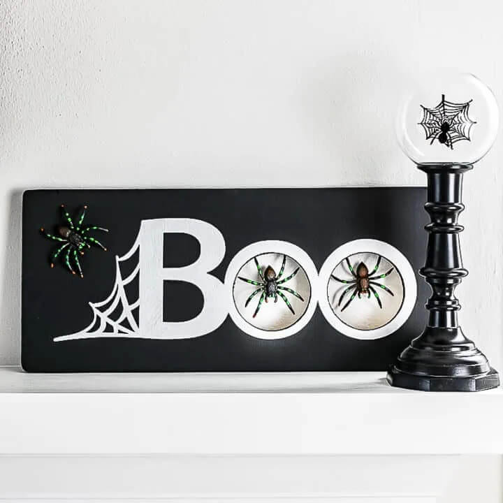 Simple black and white boo sign decorated with spiders, with a black candlestick.