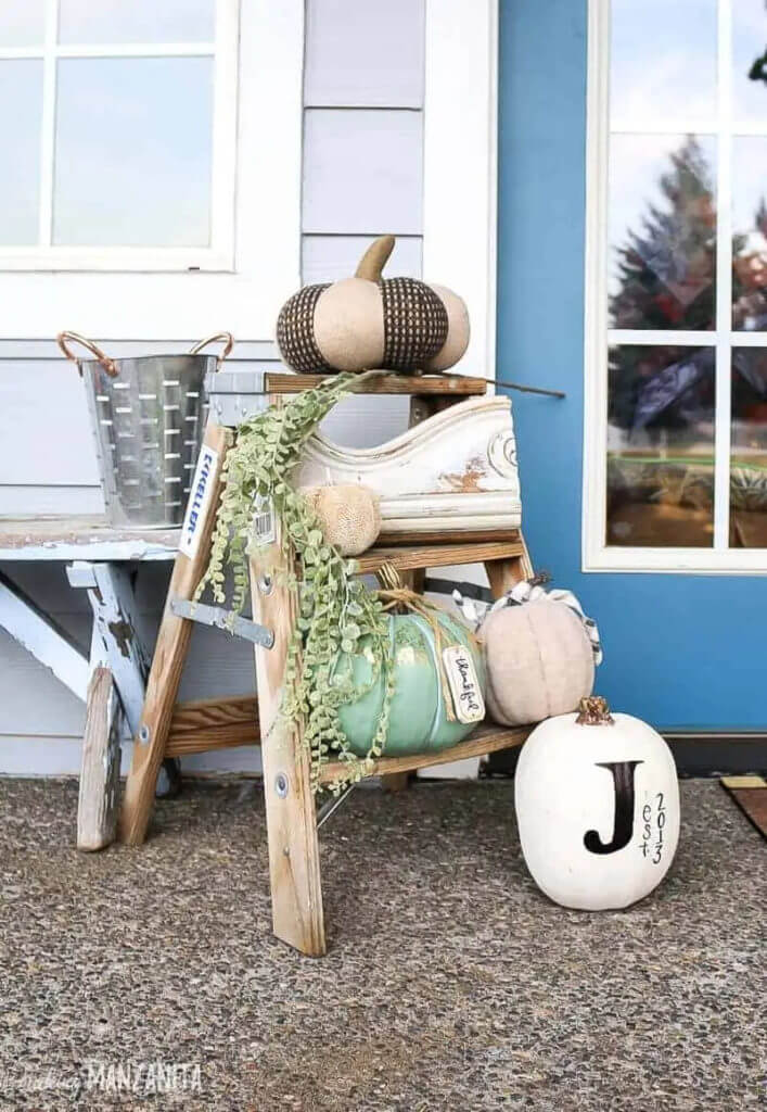simple black and white pumpkin decorations on a small ladder on front porch.