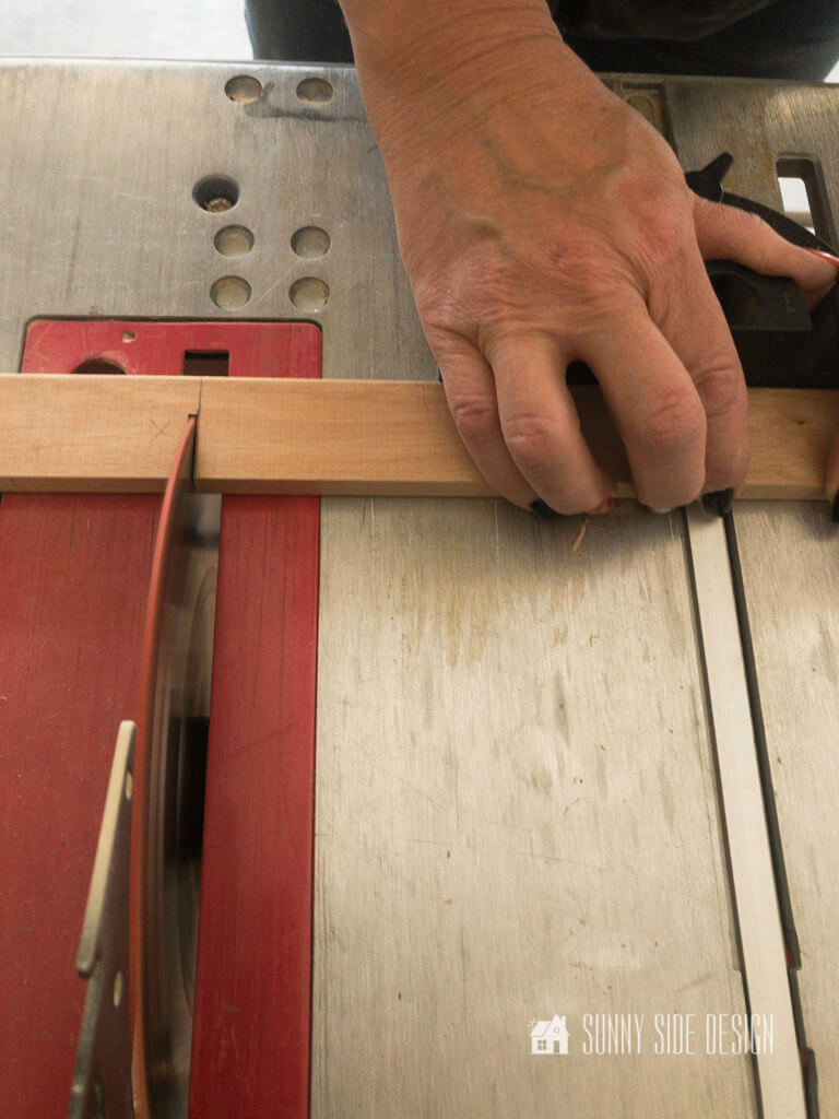 Woman's hand at table saw cutting wood trim.