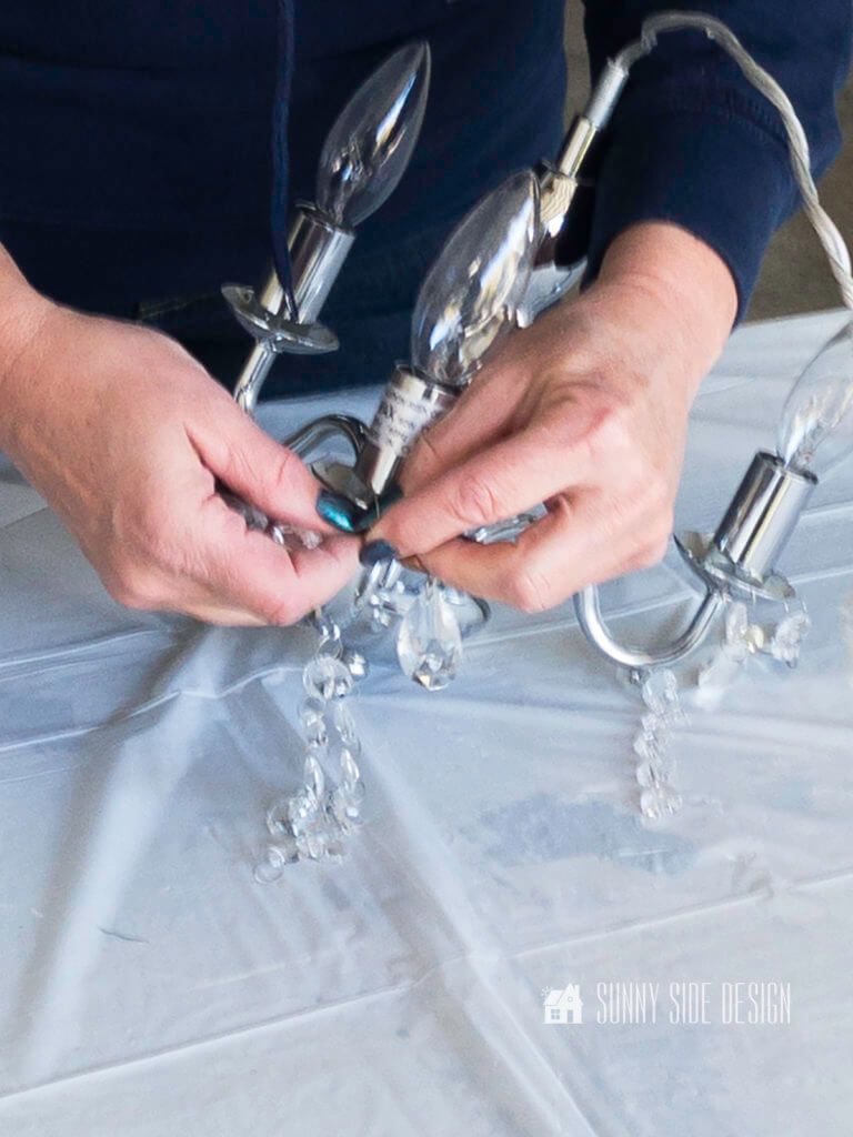 Woman's hand removing crystals from a thrift store chandelier.
