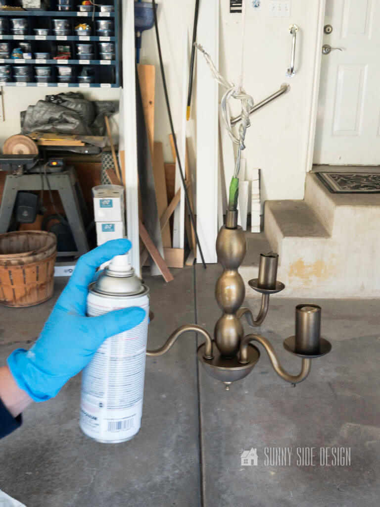 Woman's hand applying gold spray paint to thrift store chandelier for an update for a laundry room light fixture.