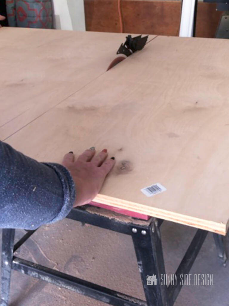 Woman's hand pushing plywood on a table saw. Cutting wood to the depth of the laundry room folding table.