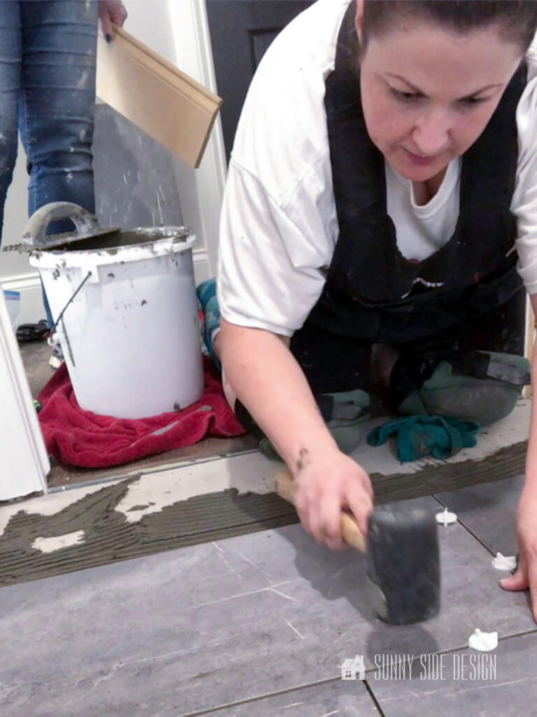 Woman installing tile, tapping tile with a rubber mallet and inserting white tile spacers